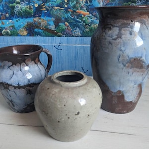 May include: Three ceramic vases of different sizes and shapes. The largest is a tall vase with a wide opening, the middle is a small round vase, and the smallest is a pitcher. The vases have a brown and blue glaze.