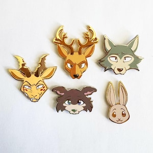 May include: Five metal enamel pins featuring stylized animal heads. The collection includes a yellow gazelle, a brown deer with gold antlers, a grey wolf, a dark brown dog, and a light brown rabbit, all outlined in polished gold metal.