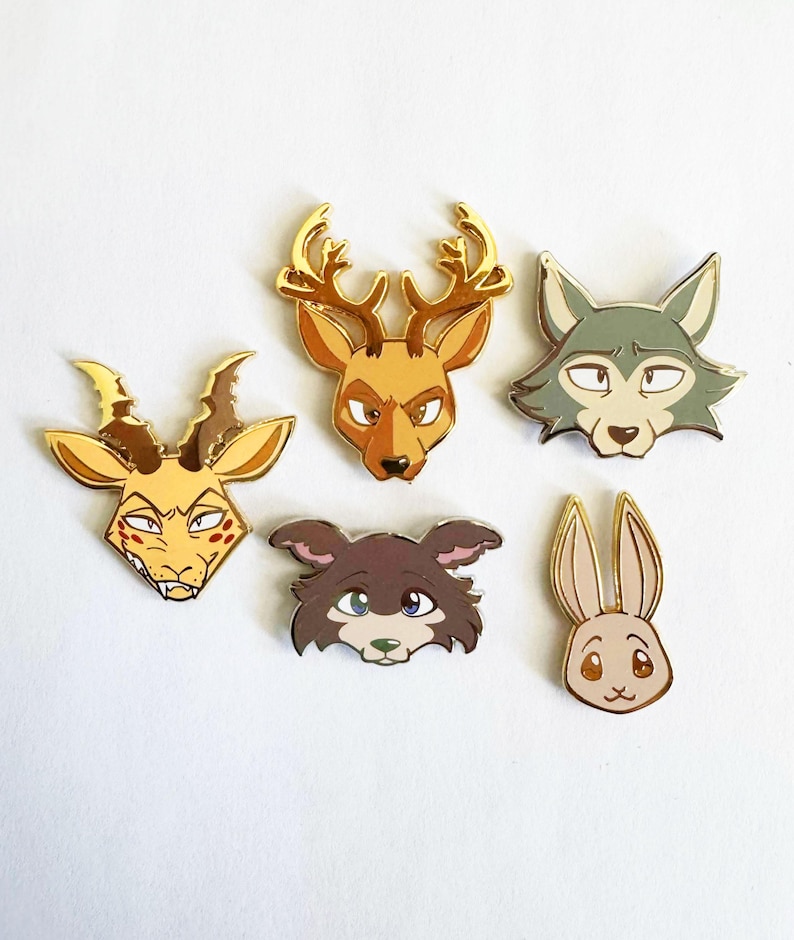 May include: Five metal enamel pins featuring stylized animal heads. The collection includes a yellow gazelle, a brown deer with gold antlers, a grey wolf, a dark brown dog, and a light brown rabbit, all outlined in polished gold metal.
