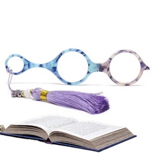 May include: Round reading glasses with a blue and white marbled pattern, a lavender tassel, and an open book with blue covers. The glasses have a unique, elongated frame.
