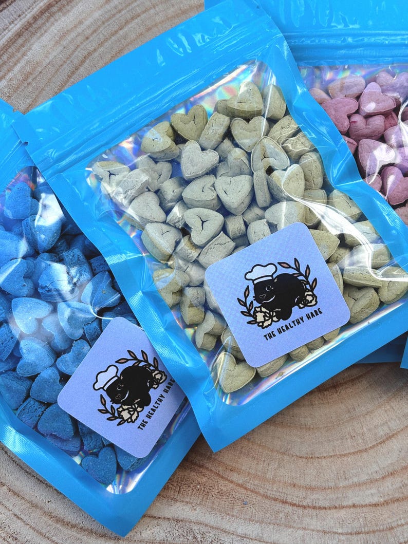 May include: Several clear plastic bags filled with heart-shaped treats in various colors. Each bag has a blue border and a square label with a black rabbit wearing a chef's hat and the text "THE HEALTHY HARE".
