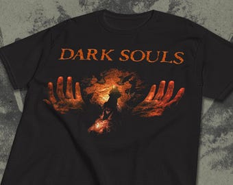 May include: Black t-shirt with the words "DARK SOULS" in orange, above a graphic of outstretched hands and a central figure. The graphic has a fiery, textured appearance.