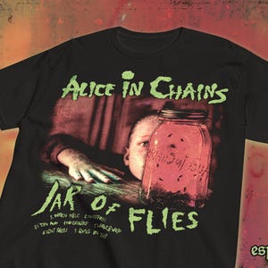 May include: Black t-shirt featuring the band name "Alice in Chains" in green, with "Jar of Flies" below. The design includes a jar with insects and a child's face. Song titles are listed below the jar.