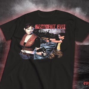Puede incluir: Camiseta negra con un gráfico del videojuego Resident Evil: Code Veronica. El diseño incluye dos personajes con armas. El texto "Resident Evil Code Veronica" está impreso en la parte superior.