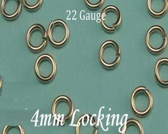 Op de afbeelding: Een verzameling zilverkleurige metalen springringen, elk met een kleine opening. De tekst 22 Gauge en 4mm Locking is zichtbaar tussen de verspreide ronde onderdelen, die zijn ontworpen voor het maken van sieraden en het verbinden van stukken.