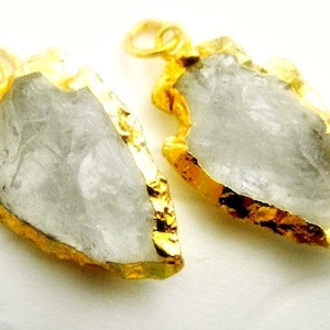 May include: Two gold-plated arrowhead pendants with clear quartz crystals. The arrowheads are irregular in shape and have a rough, natural texture.