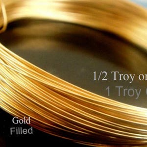 May include: Close-up of a coil of gold-filled wire. The wire is a bright, shiny gold color. Text on the image reads "1/2 Troy or 1 Troy Oz" and "Gold Filled". This wire is likely used for jewelry making and crafting.