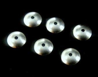May include: Six silver-toned metal round beads with a small hole in the center. The beads are slightly domed and have a shiny finish.