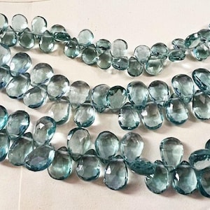 Puede incluir: Una hebra de cuentas de piedras preciosas facetadas de color azul claro. Las cuentas tienen forma de lágrima y están enhebradas en un hilo transparente.