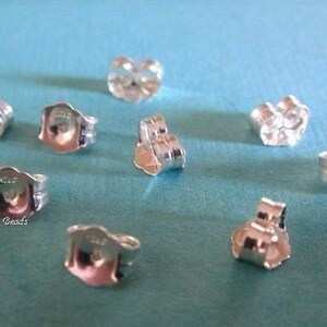 May include: Eight silver earring backs on a blue surface. The backs are designed to fit over a post earring.