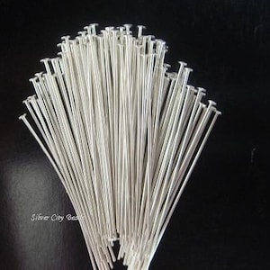 May include: A bunch of silver head pins, also known as jewelry making head pins, are arranged in a fan shape. The pins are all the same size and have a small, round head on one end.