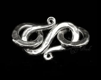 May include: Silver clasp with a unique, intricate design. The clasp is made of two interlocking loops, each with a smooth, rounded finish.