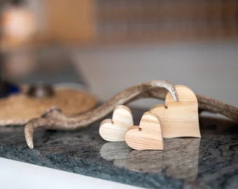 May include: Three wooden heart shapes of varying sizes, arranged on a gray granite surface with a brown antler in the background.
