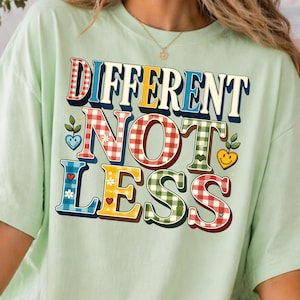 Könnte beinhalten: Hellgrünes T-Shirt mit dem Schriftzug "DIFFERENT NOT LESS" in bunten, gemusterten Buchstaben. Der Text weist eine Mischung aus Karomustern, floralen Mustern und unifarbenen Farben auf. Das Shirt ist ein lässiger, bequemer Stil.