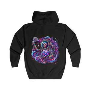 Könnte beinhalten: Schwarzer Hoodie mit einer farbenfrohen Illustration eines Affen-Astronauten, der eine leuchtende Kugel und einen Lutscher hält. Der Affe trägt einen Raumanzug und ist von wirbelnden Wolken umgeben.