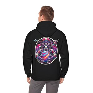 Könnte beinhalten: Schwarzer Kapuzenpullover mit einem bunten Grafikdruck eines Affen-Astronauten, der einen Planeten hält. Der Affe trägt einen Helm und hat ein schädelartiges Gesicht.
