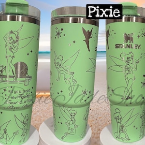 Puede incluir: Un vaso de acero inoxidable verde con tapa y asa. El vaso presenta un diseño de Campanilla y la cita "Todo lo que necesitas es fe, confianza y un poco de polvo de hada".