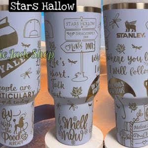 May include: A light blue stainless steel tumbler with gold lettering. The tumbler features various designs and text, including "Stars Hollow", "Life's short. Talk last." and "Where you lead I will follow".
