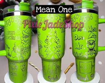 Puede incluir: Tres vasos de acero inoxidable en color verde lima brillante con asas y tapas. Cada uno presenta ilustraciones navideñas grabadas con láser en plata, incluyendo un personaje, árboles de Navidad, regalos y el texto Merry Grinchmas y You're a Mean One Mr. Grinch.