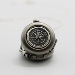 May include: A silver compass charm with a detailed design. The compass is attached to a silver chain.
