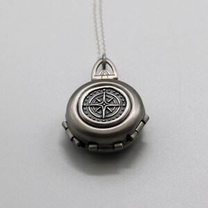 May include: A silver locket necklace with a compass design. The compass has a black face with a silver star in the center.