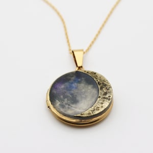 Puede incluir: Un collar de oro con un dije en forma de media luna. El dije tiene una imagen con tem&aacute;tica de galaxia en su interior.