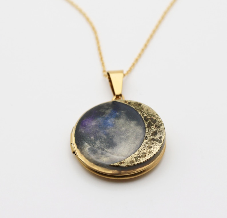 Puede incluir: Un collar de oro con un dije en forma de media luna. El dije tiene una imagen con tem&aacute;tica de galaxia en su interior.