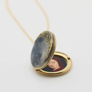 Puede incluir: Un collar con un medall&oacute;n de oro con un dise&ntilde;o de media luna en la parte delantera. El medall&oacute;n est&aacute; abierto, revelando un retrato pintado de una mujer en el interior.