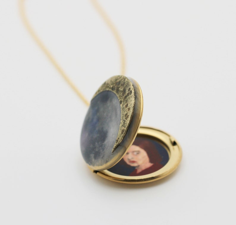 Puede incluir: Un collar con un medall&oacute;n de oro con un dise&ntilde;o de media luna en la parte delantera. El medall&oacute;n est&aacute; abierto, revelando un retrato pintado de una mujer en el interior.
