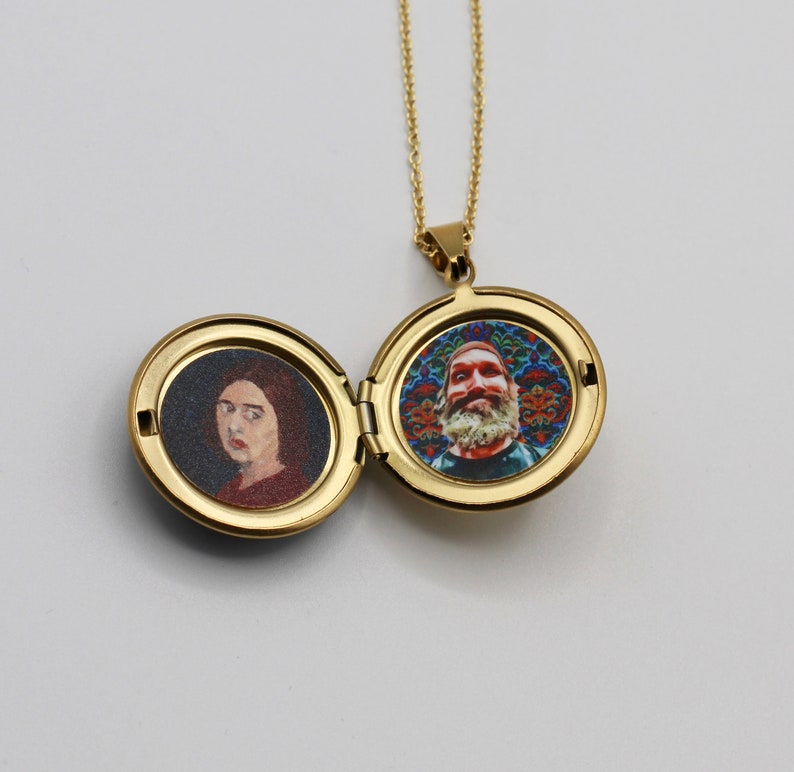 Puede incluir: Un collar con un medall&oacute;n de oro que contiene dos retratos. En un lado, una mujer con el pelo corto y casta&ntilde;o, en el otro, un hombre con barba sobre un fondo colorido.