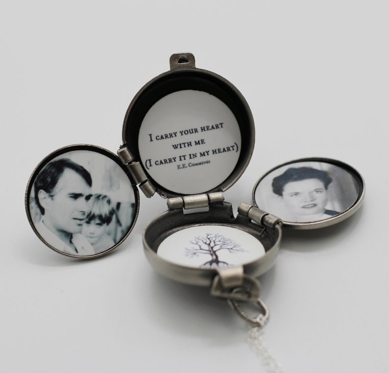Peut inclure: Un m&eacute;daillon argent&eacute; ouvert, r&eacute;v&eacute;lant trois compartiments. &Agrave; l'int&eacute;rieur, des photographies en noir et blanc d'un homme et d'un enfant, d'une femme et d'une illustration d'arbre. Le compartiment central porte la citation "I carry your heart with me" de E.E. Cummings.