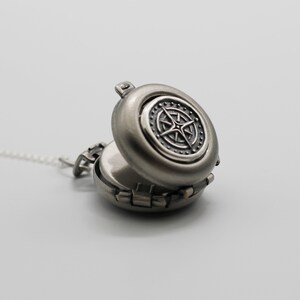 May include: A silver locket necklace with a compass design on the front. The locket is open, revealing a blank interior.