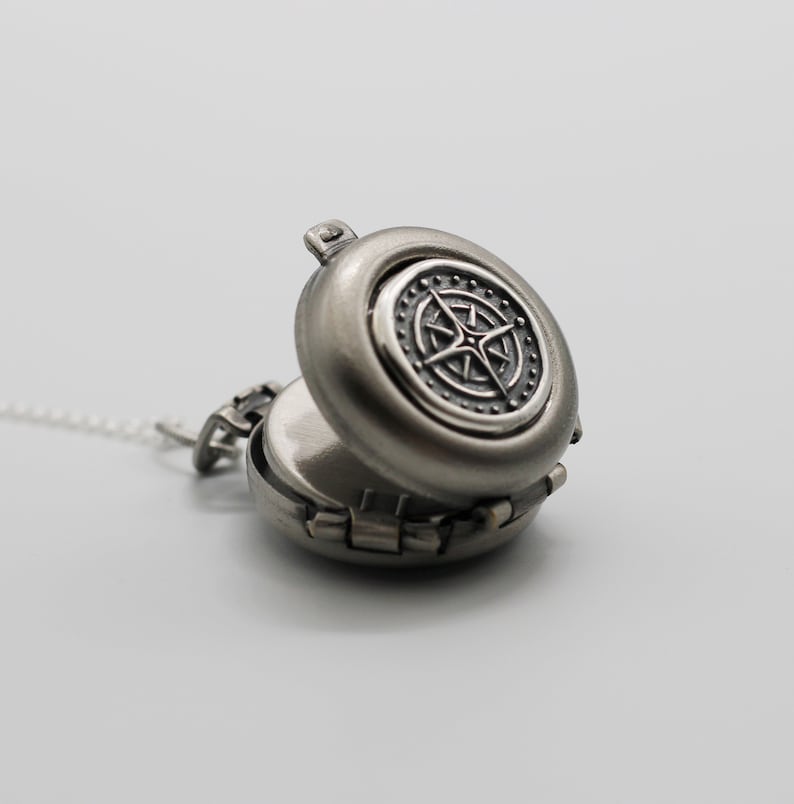 May include: A silver locket necklace with a compass design on the front. The locket is open, revealing a blank interior.