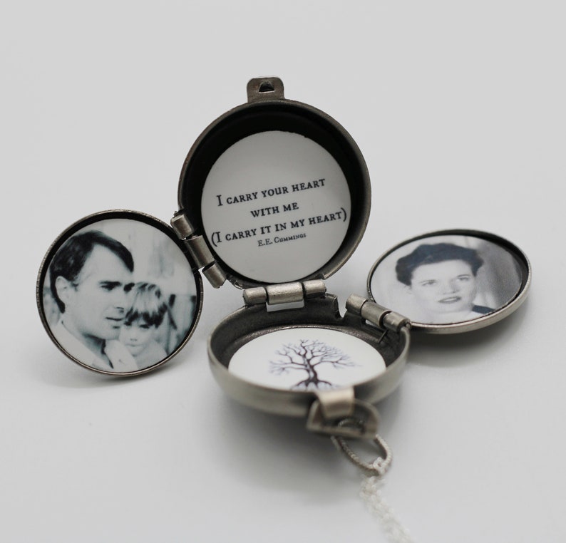 May include: A silver locket necklace with a hinged lid. The locket is open, revealing a black and white photo of a man and a child. The other side of the locket has a black and white photo of a woman. The locket has a quote inside: "I carry your heart with me (I carry it in my heart) E.E. Cummings".