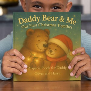 May include: A children's book titled "Daddy Bear & Me" with the subtitle "Our First Christmas Together." The cover features illustrations of two bears, one wearing a Santa hat and scarf. The book is held by a person.