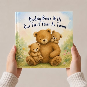May include: A children's book titled "Daddy Bear & Us Our First Year As Twins" held by hands. The cover features an illustration of a large brown bear with two smaller bears. The background has a soft, watercolor-style landscape with flowers.