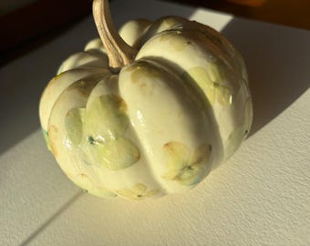 May include: A white ceramic pumpkin decorated with pressed green and blue flowers. The pumpkin has a smooth, glossy finish.