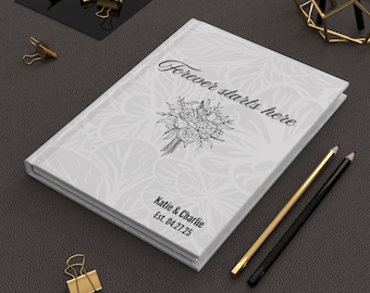 May include: White hardcover journal with a floral design and the text "Forever starts here" on the front cover. The journal also has the text "Katie & Charlie Est. 04.27.25" on the bottom of the front cover.