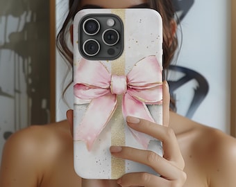 Puede incluir: Funda de teléfono blanca con un diseño de acuarela de un lazo rosa y detalles dorados. La funda tiene una franja vertical dorada y un fondo moteado. La funda del teléfono tiene un módulo de cámara con tres lentes.