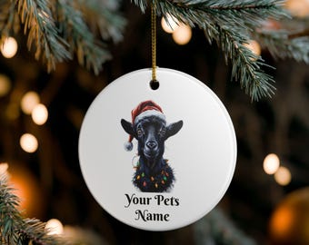 May include: White ceramic Christmas ornament featuring a black goat wearing a Santa hat and string lights. The text "Your Pets Name" is printed below the goat. The ornament hangs from a gold string.