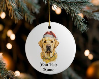Könnte beinhalten: Weißer, runder Weihnachtsschmuck mit einem gelben Labrador Retriever, der einen Weihnachtsmannhut und eine Lichterkette trägt. Der Text "Your Pets Name" ist darunter gedruckt. Der Schmuck hängt an einem goldenen Faden.