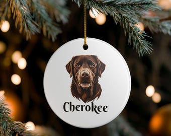 Könnte beinhalten: Runder, weißer Keramik-Weihnachtsschmuck mit einer detaillierten Illustration eines braunen Labrador Retrievers. Der Name des Hundes, "Cherokee", ist darunter aufgedruckt. Ein goldener Faden ist zum Aufhängen befestigt.