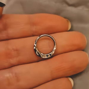 May include: A silver-colored, textured hoop earring. The earring has an irregular, hammered design. The word "lusi" is printed in black, with the word "SELLS" below it.