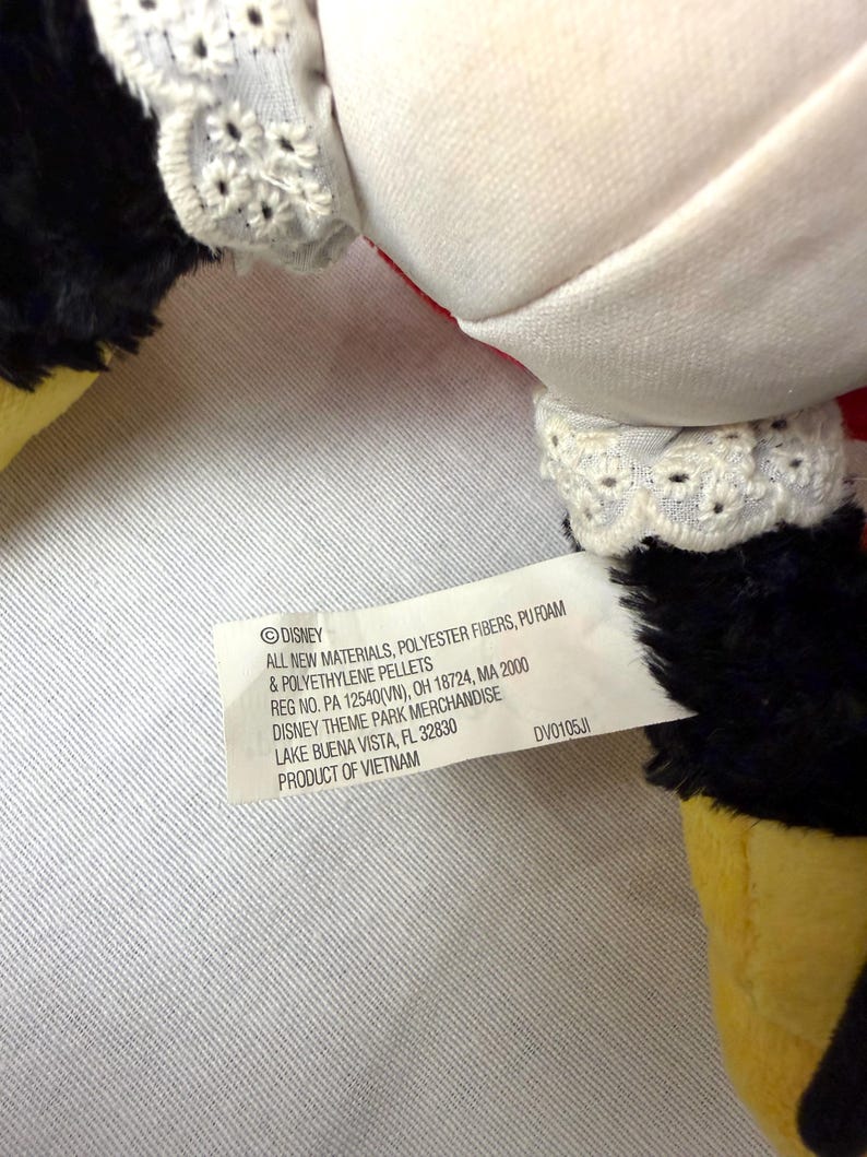 May include: Close-up of a plush toy with white fabric, black fur, and yellow feet. The toy has white lace trim and a tag with text including "DISNEY" and "PRODUCT OF VIETNAM".