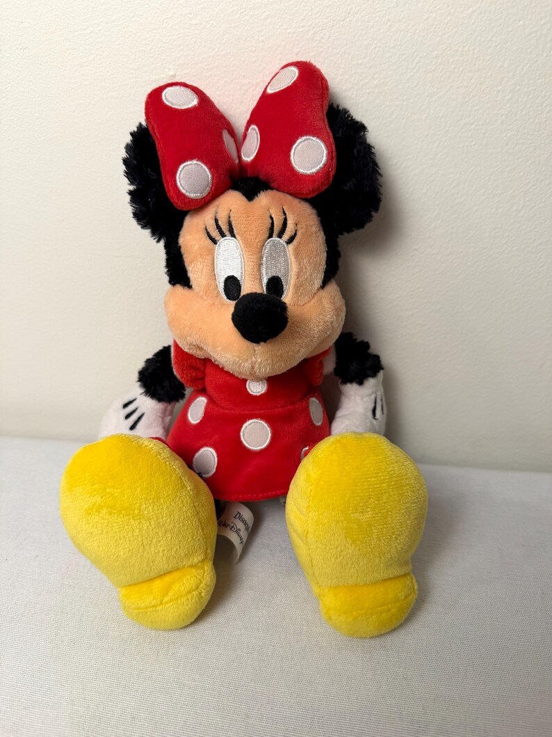 May include: A plush Minnie Mouse doll, with a red dress and white polka dots, a matching bow, and yellow shoes. The doll has black fur, white gloves, and a smiling face. A classic Disney character.