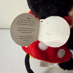 May include: A soft Mickey Mouse toy, featuring a red and white polka dot outfit. The toy has a black head and tail, with a tag stating "Made exclusively for the Walt Disney Theme Parks and Resorts."