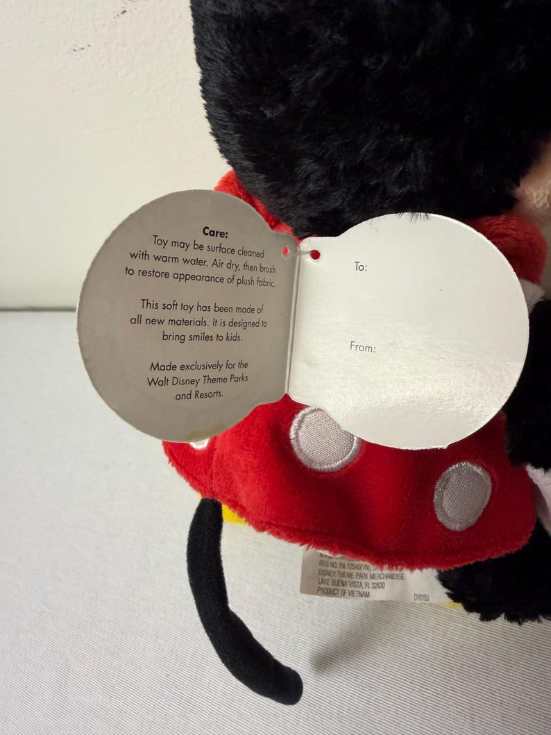May include: A soft Mickey Mouse toy, featuring a red and white polka dot outfit. The toy has a black head and tail, with a tag stating "Made exclusively for the Walt Disney Theme Parks and Resorts."