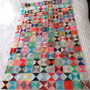 May include: A colorful patchwork quilt made from a variety of fabrics in shades of red, blue, green, pink, and brown. The quilt is made up of small squares, each with a different pattern. The quilt is laid out on a white bedspread.