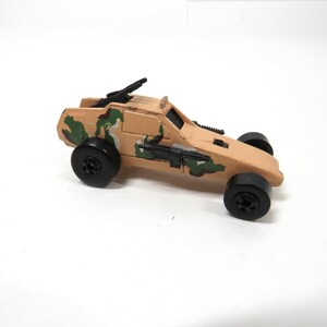 Peut inclure: Un véhicule militaire jouet de couleur beige avec des roues noires et des détails de camouflage. La voiture jouet a un canon monté sur le dessus et un canon peint sur le côté. Le jouet est en plastique.