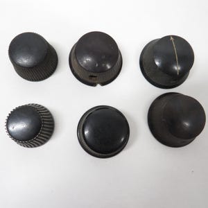 May include: Six vintage black knobs with various ridged and textured designs. One knob has a white arrow. These knobs are likely for electronics or appliances.
